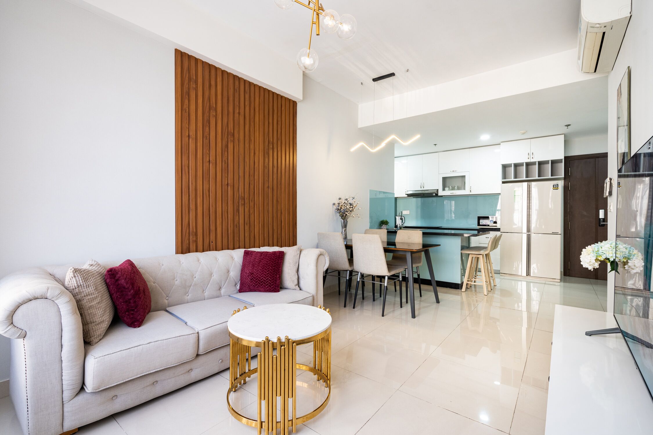 Un salon moderne avec un canapé blanc, une table ronde dorée et un mur d’accent en bois.