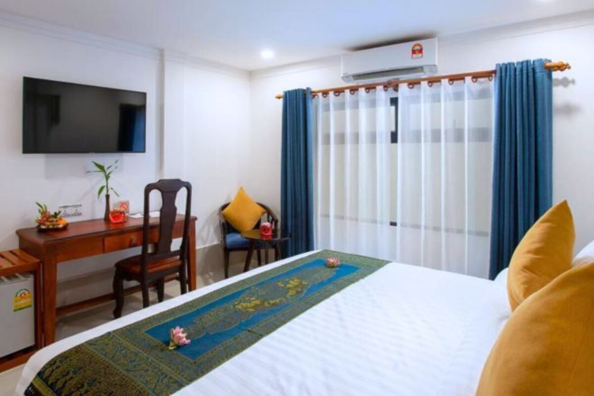 Habitación de hotel con cama, escritorio, silla, televisor y ventana con cortinas.