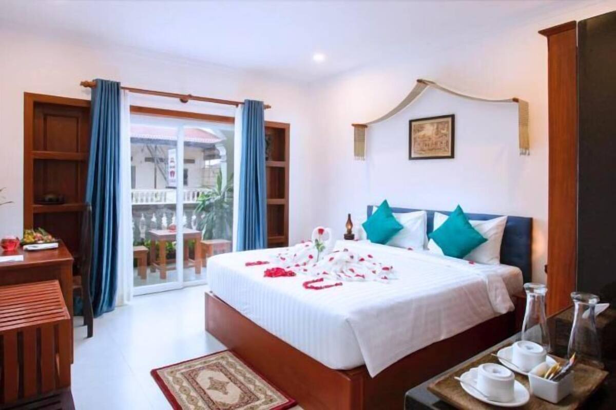 A hotel room with a bed, a desk, a chair, a small table with a tray, and a view of the outside.
