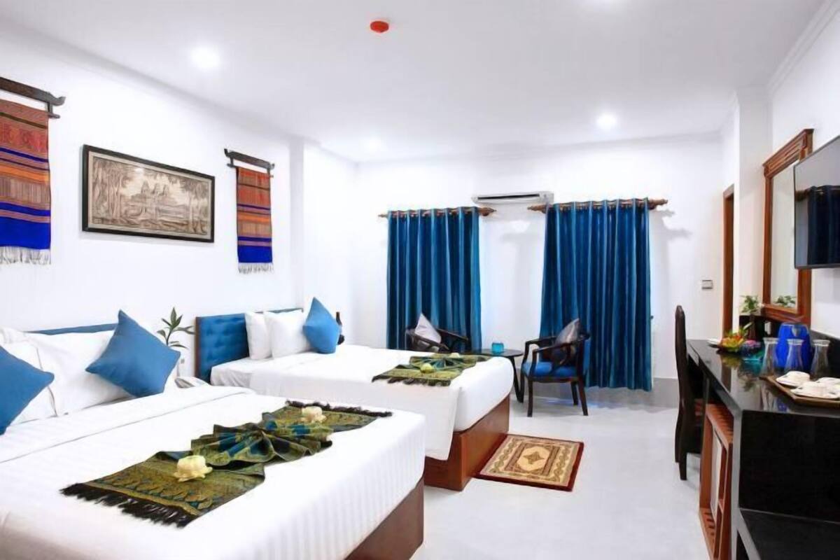 A hotel room with two beds, a desk, a chair, and a TV.