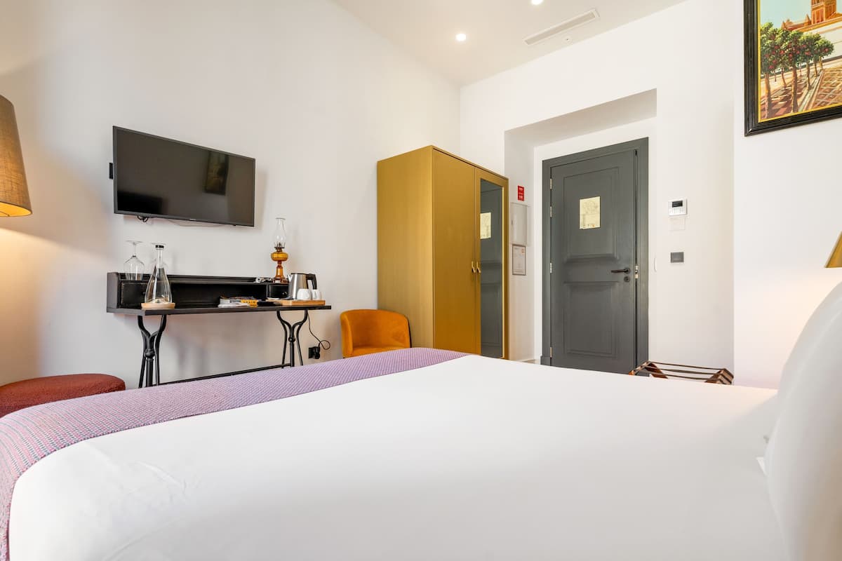 A hotel room with a bed, a desk with a chair, a television, and a wardrobe.
