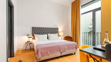 Een hotelkamer met een bed, een bureau, een stoel, een lamp en een balkon met gordijnen.