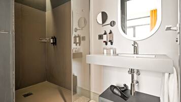 Un baño moderno con ducha envuelta en vidrio, un lavamanos blanco y un espejo.