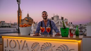 A bar counter with a sign reading "JOYA DEL CASCO," two glasses of red drink, and bottles of liquor. - Joya del Casco Boutique Hotel (Seville)