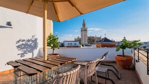 A rooftop terrace with a wooden table and chairs, potted plants, and a view of a historic tower. - Joya del Casco Boutique Hotel (Seville)