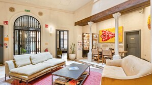 A spacious lobby with a sofa, armchairs, and a coffee table. There is a bookshelf with books and a large painting on the wall. - Joya del Casco Boutique Hotel (Seville)