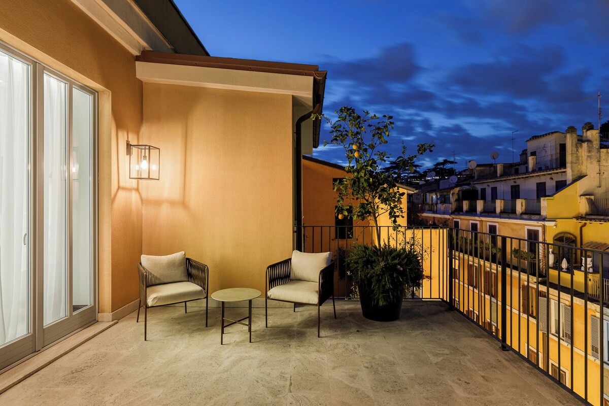 A balcony with two chairs and a table, a potted plant, and a view of neighboring buildings.