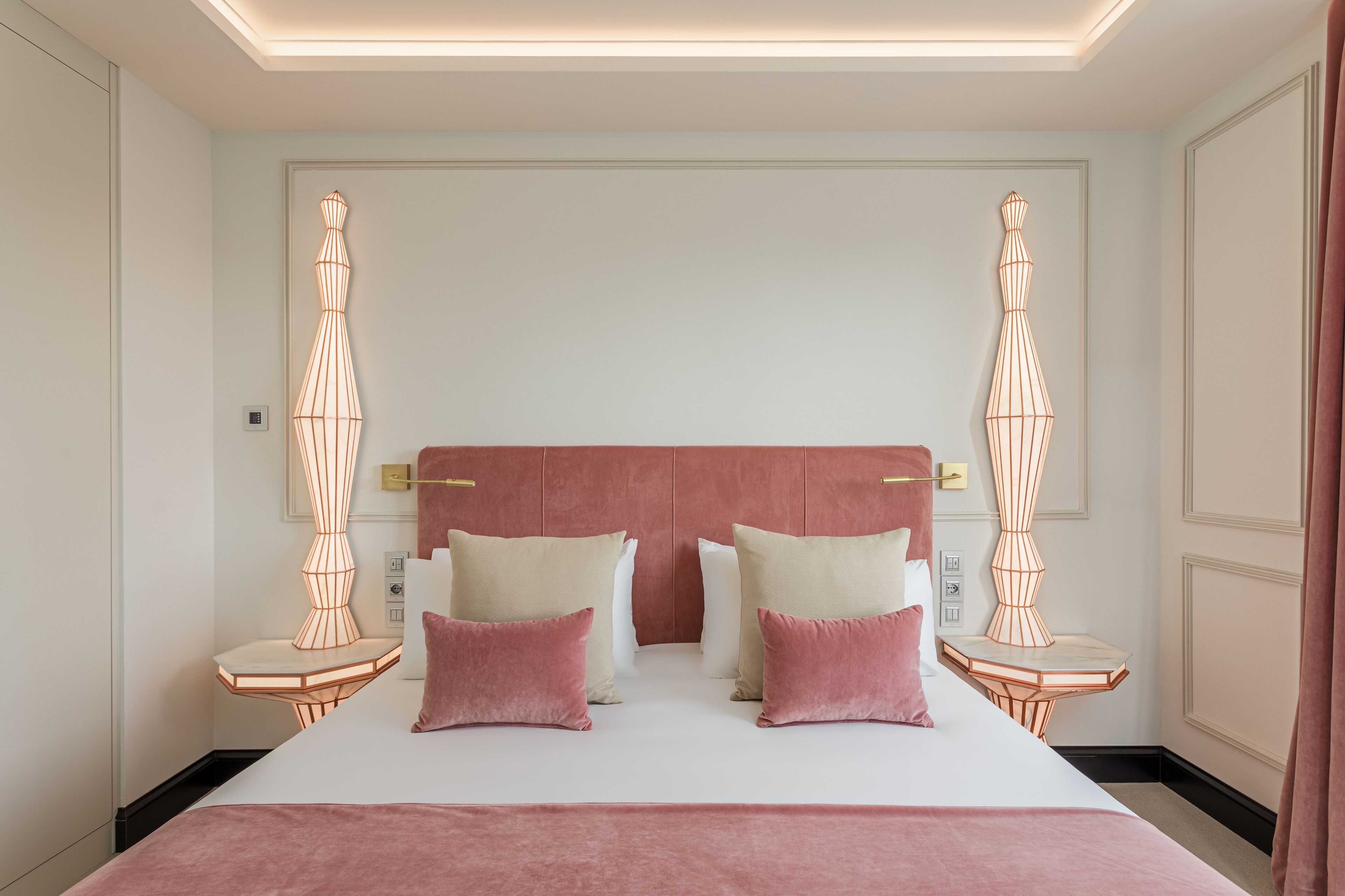 Habitación de hotel moderna con una cama grande, dos mesitas de noche y una lámpara con un diseño geométrico único a cada lado.