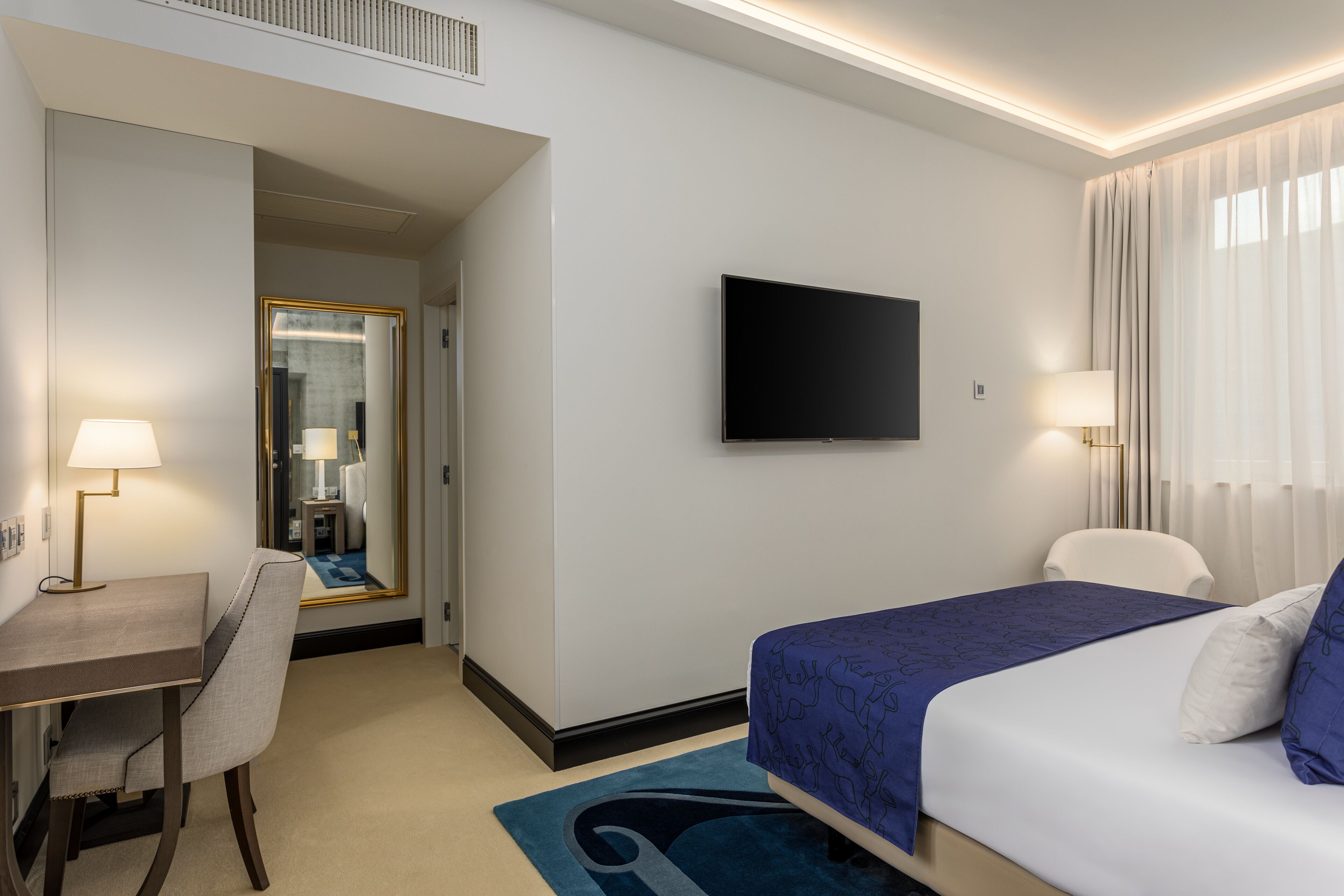 Habitació d'hotel amb llit, escriptori, cadira, televisió i mirall.