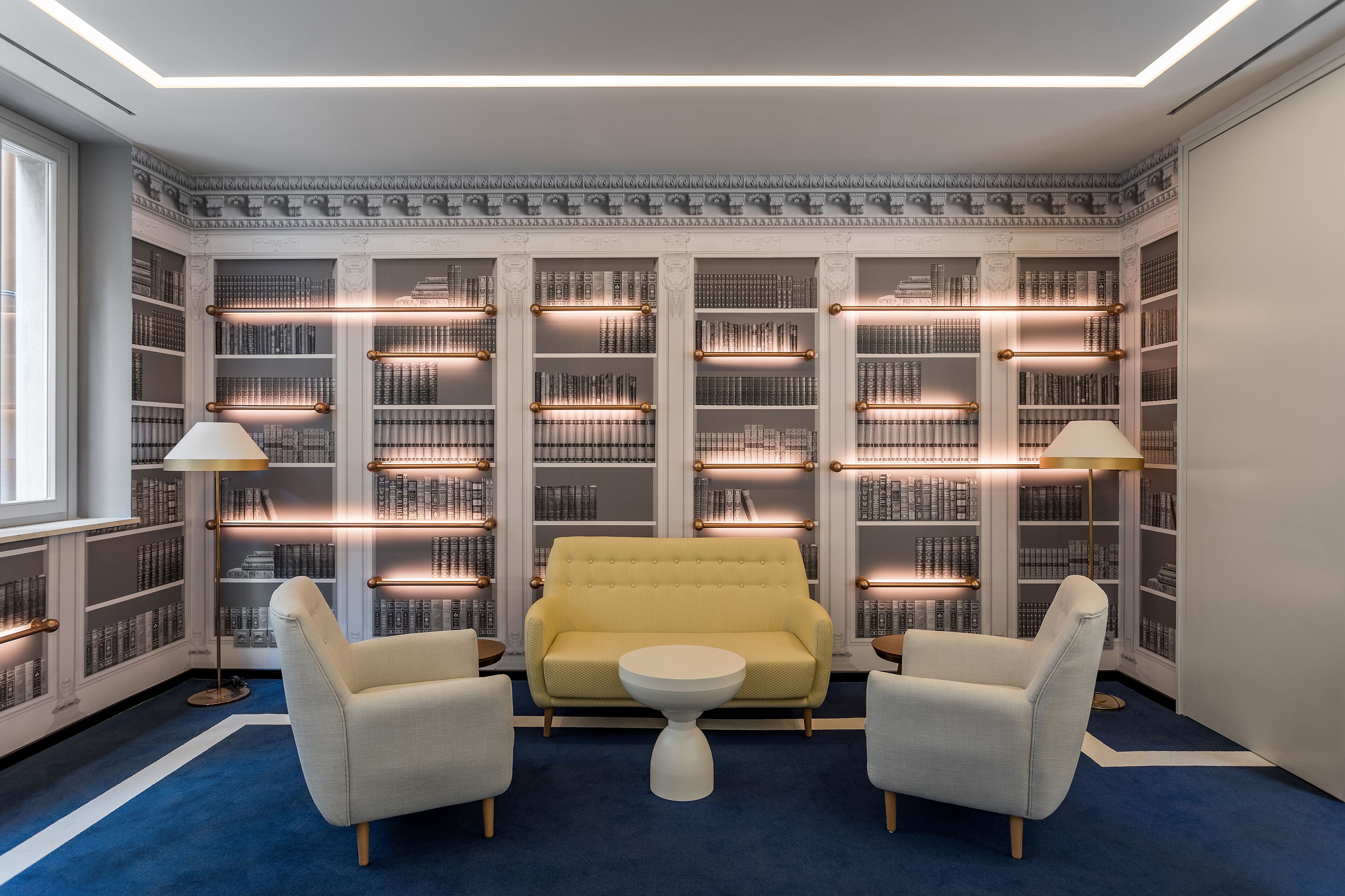 Una biblioteca con un sofá amarillo, dos sillones y una mesita.