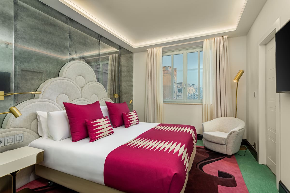 Habitació d'hotel amb un llit gran, una cadira, escriptori, televisió i finestra amb vista a la ciutat.