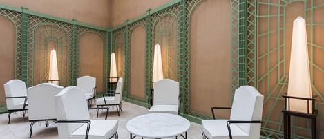 A courtyard with white chairs and tables, green lattice walls, and hanging plants.