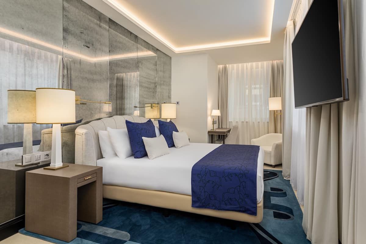 Habitació d'hotel moderna amb un llit gran, dues taules de nit amb làmpades, un televisió de pantalla plana i un gran mirall a la paret.