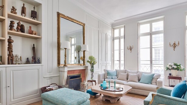 Un salon spacieux doté d’un parquet en point de Hongrie, d’un grand miroir, d’une cheminée, d’un canapé et d’une table basse.