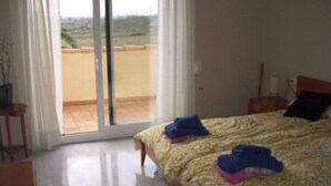 Un dormitorio con cama, mesita de noche, lámpara y vistas a un balcón.