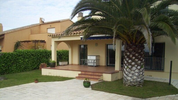 Una casa con porche cubierto, una palmera y un jardín bien cuidado.