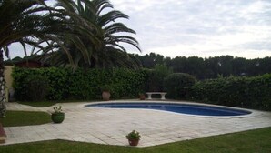 Una piscina rodeada por un patio empedrado, palmeras y un seto.