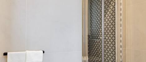 A modern bathroom with a glass shower enclosure, a white towel hanging on a black towel rack, and patterned tiles on the walls.