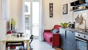 Una cocina moderna con un sofá rojo, una mesa de comedor y sillas. Hay un florero con flores sobre la mesa, y muebles de cocina con electrodomésticos.