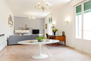 Una sala moderna con una mesa redonda blanca, un sofá gris, un televisor y una araña.
