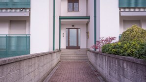 A building with a central entrance, a small window above the door, and a brick pathway leading to the entrance. - Buttrio Appartamento nel Verde (Buttrio)