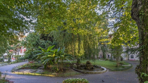 A circular courtyard with a fountain, surrounded by trees and a paved walkway. - Ricasoli Garden Modern Apartment (Udine)