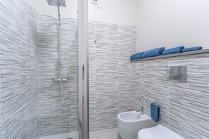 Une salle de bain moderne avec une douche à parois de verre, un lavabo blanc et un porte-serviettes avec des serviettes bleues.
