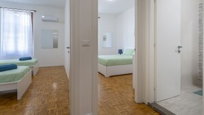 A room with two beds, a wooden floor, a white door, and a mirror on the wall. - Ricasoli Garden Modern Apartment (Udine)