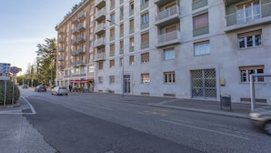 A multi-story residential building with balconies, a street in front, and a clear sky.