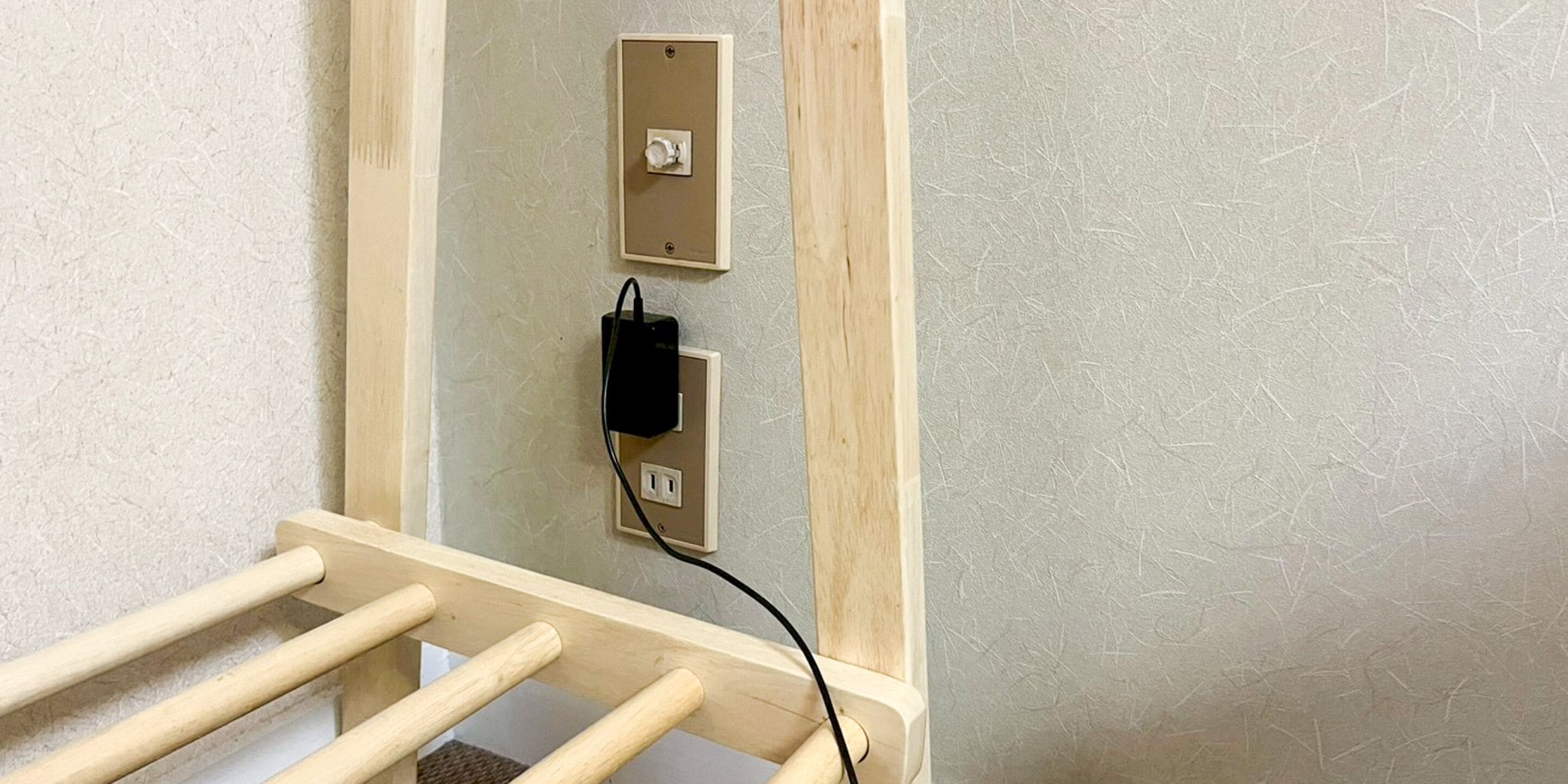 A wooden bed frame with a mattress partially visible, a wall-mounted electrical outlet, and a switch.