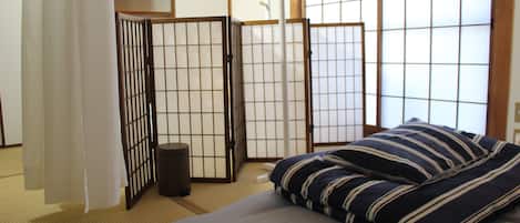 Una habitación tradicional japonesa con suelo de tatami, una cama baja con ropa de cama a rayas y puertas correderas shoji.
