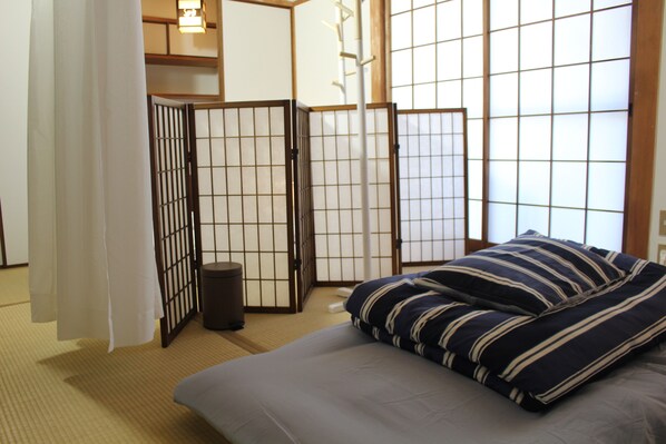 A traditional Japanese-style room with tatami flooring, a low bed with striped bedding, and shoji screens.