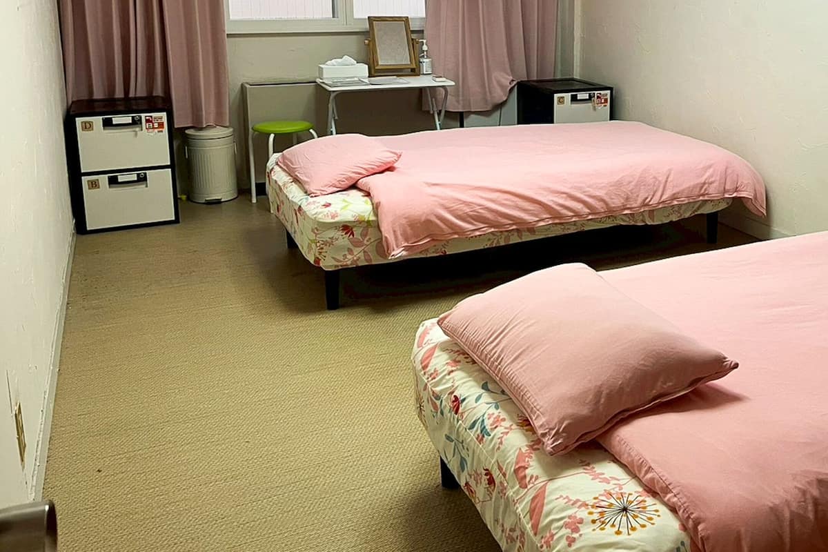 A bedroom with two beds, a desk, and a trash bin.