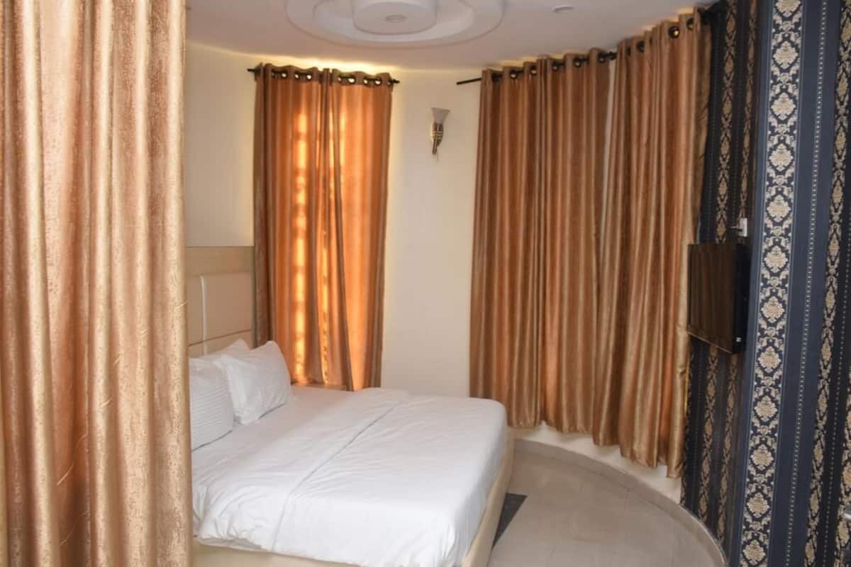 A hotel room with a bed, curtains, a wall-mounted TV, and patterned wallpaper.