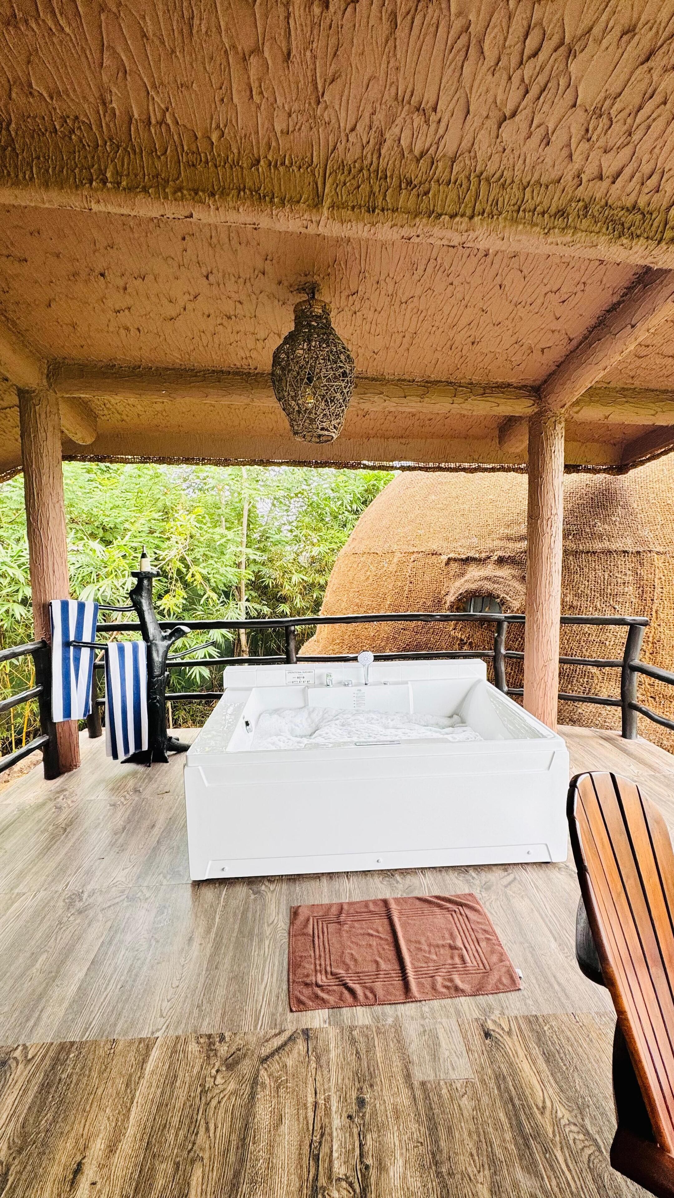 A wooden deck with a bed, a hanging lantern, and a view of greenery.