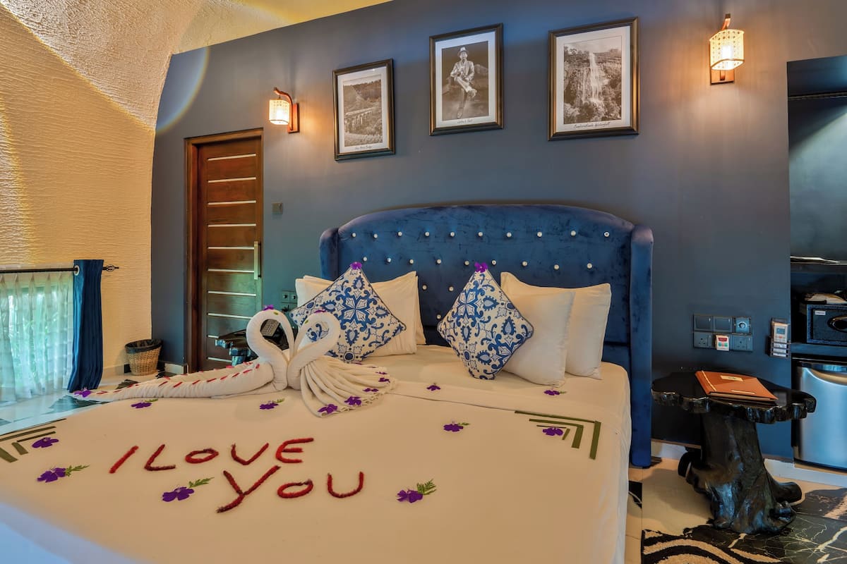 Ein Hotelzimmer mit einem Bett, das mit einem Schwanentowel und einer 'I love you'-Dekoration versehen ist, einem blauen Kopfteil und gerahmten Bildern an der Wand.