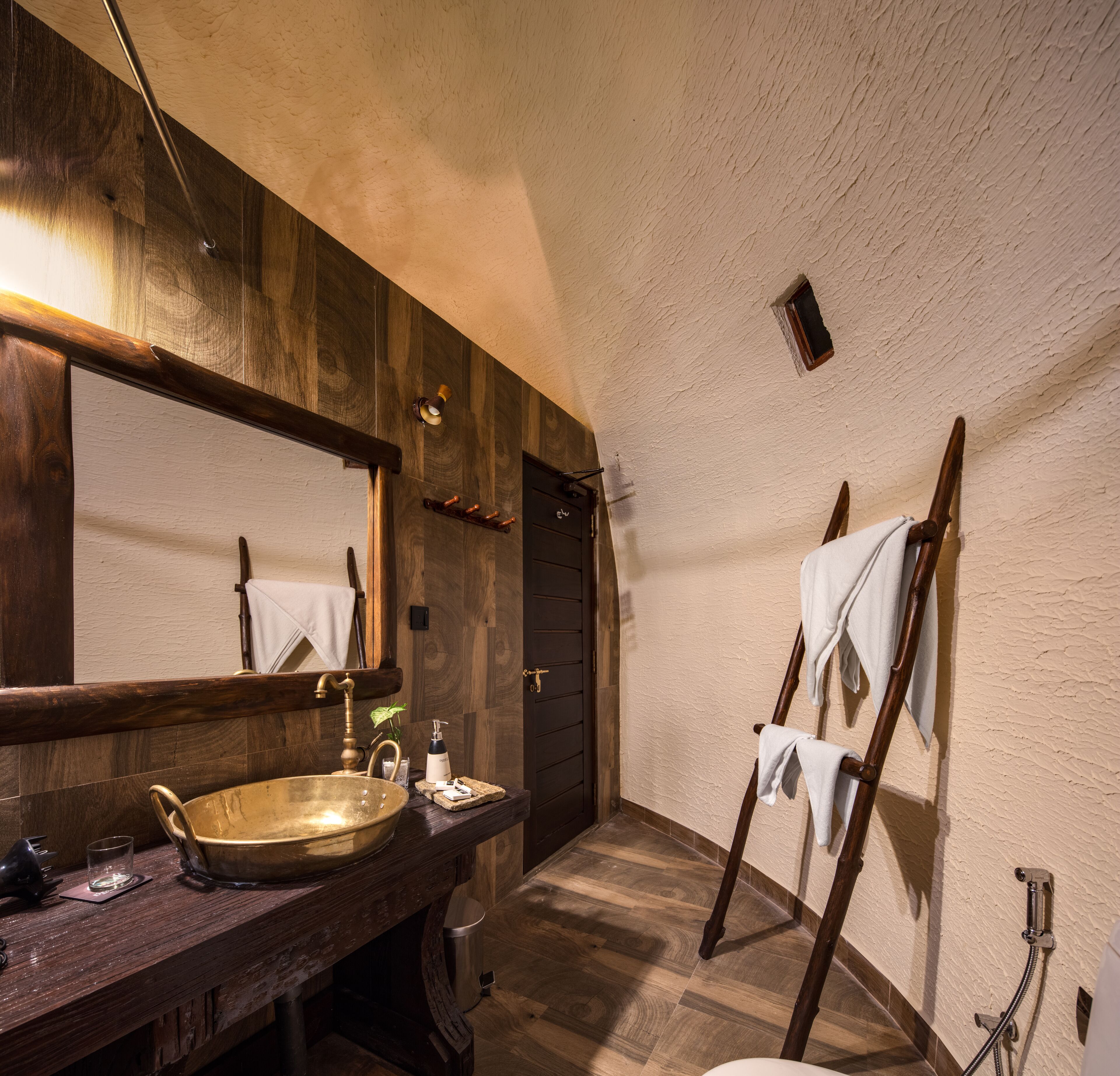 A rustic bathroom with a wooden vanity, a large mirror, a brass basin, and a towel rack.