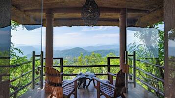 A wooden deck with a table and chairs overlooking a mountainous landscape.