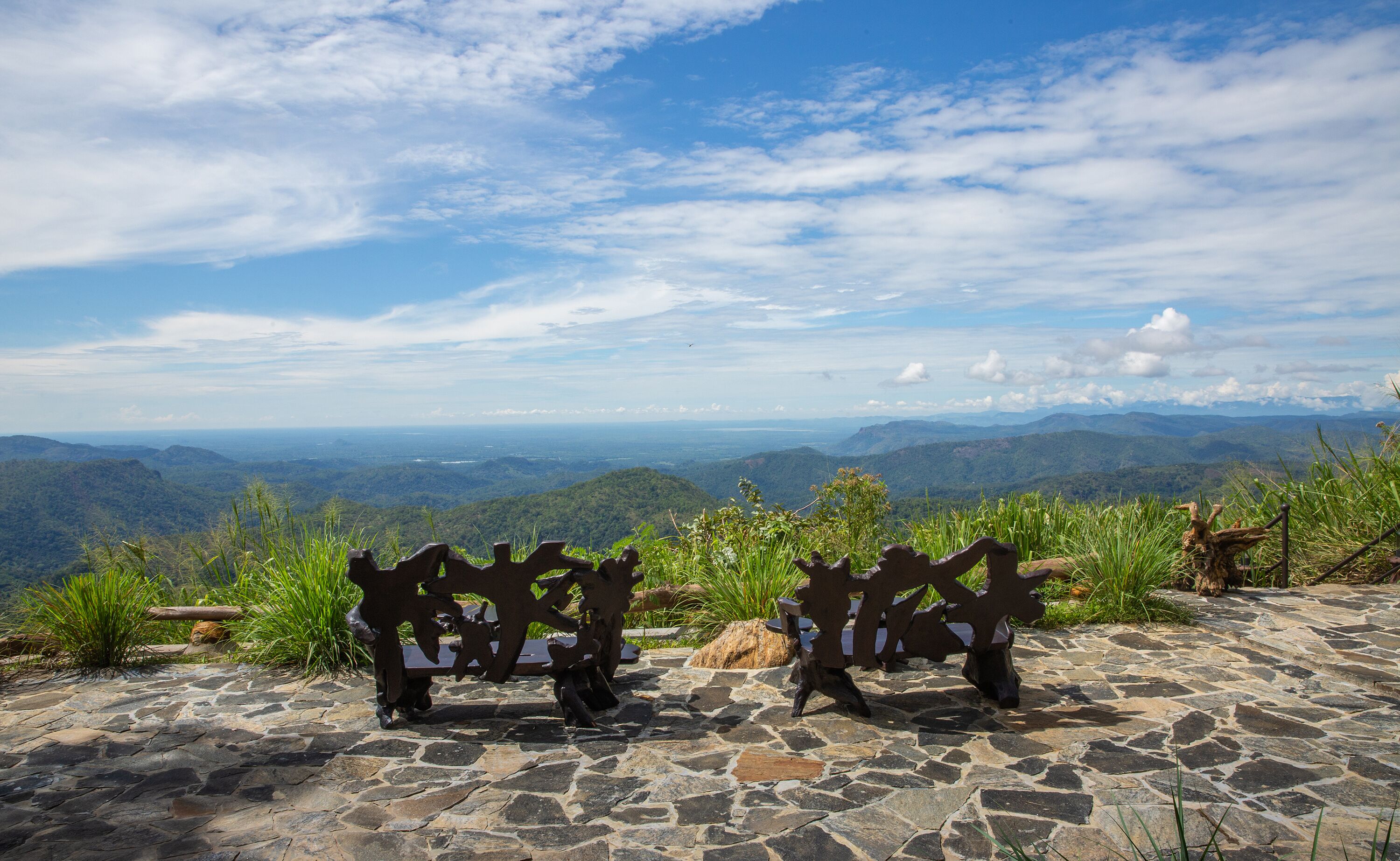 A stone bench overlooking a mountainous landscape with a clear sky.
