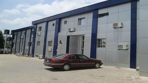 A red car parked in front of a large industrial building with multiple windows and air conditioning units. - Casa Estrella Hotel (Abuja)