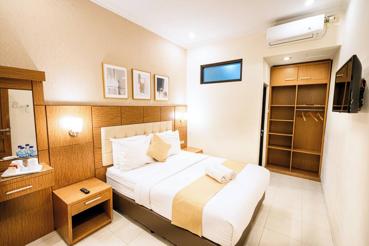 A hotel room with a bed, bedside table, wardrobe, and a flat-screen TV mounted on the wall.