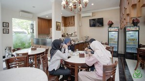 A dining area with round tables and chairs, a chandelier, and a refrigerator with beverages. - Selaras Inn Syariah (Yogyakarta)