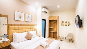 A hotel room with a large bed, a wardrobe, a TV, and a small table with a chair. - Selaras Inn Syariah (Yogyakarta)