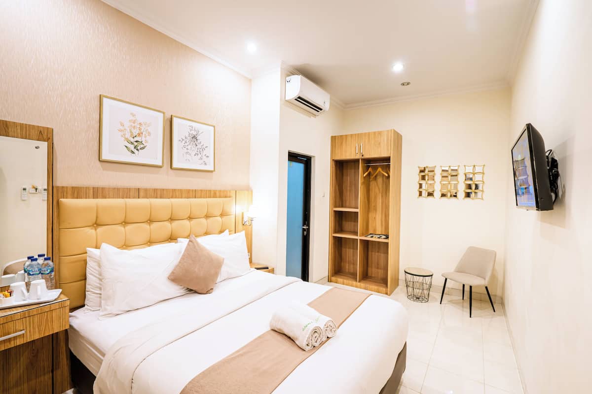 A hotel room with a large bed, a wardrobe, a TV, and a small table with a chair.