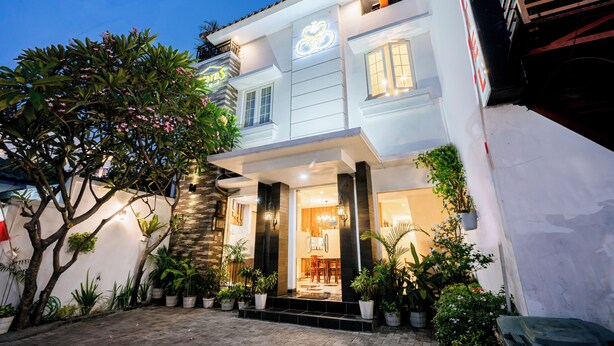 A modern two-story building with a well-lit entrance, potted plants, and a visible dining area inside. - Selaras Inn Syariah (Yogyakarta)