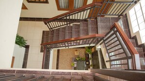 A staircase with a wooden handrail and metal balusters, leading to a landing with a tiled wall and a small plant. - Selaras Inn Syariah (Yogyakarta)