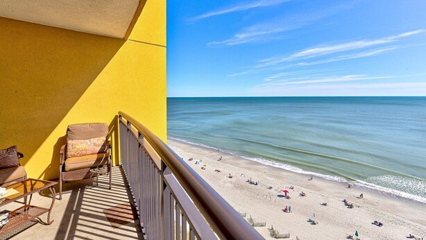 A balcony with a yellow wall, a chair, and a table. - Direct oceanfront pools hot tubs downtown Myrtle Beach (Myrtle Beach)