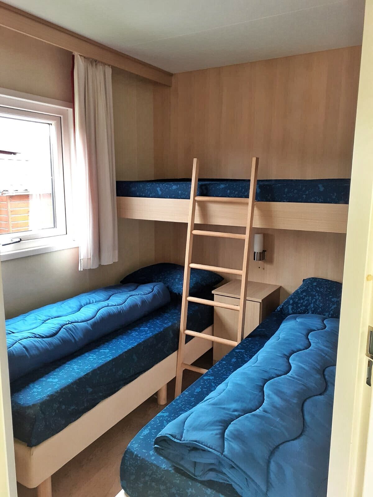Ein kleines Zimmer mit Etagenbetten, einem Fenster mit Vorhängen und einem kleinen Nachttisch.