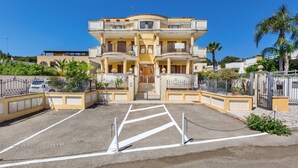 A multi-story building with balconies, a gated entrance, and a parking area.