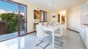 A modern kitchen with white cabinets, a dining area with a white table and chairs, and a large sliding glass door leading to a balcony.